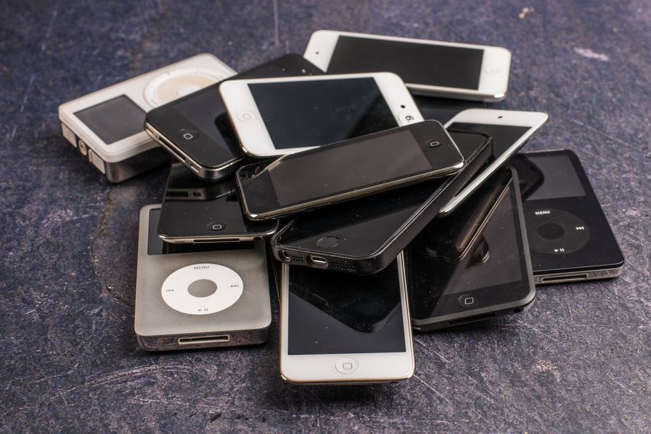 Heap of aged mobile phones with black screens and portable media players with symbols on buttons on gray background